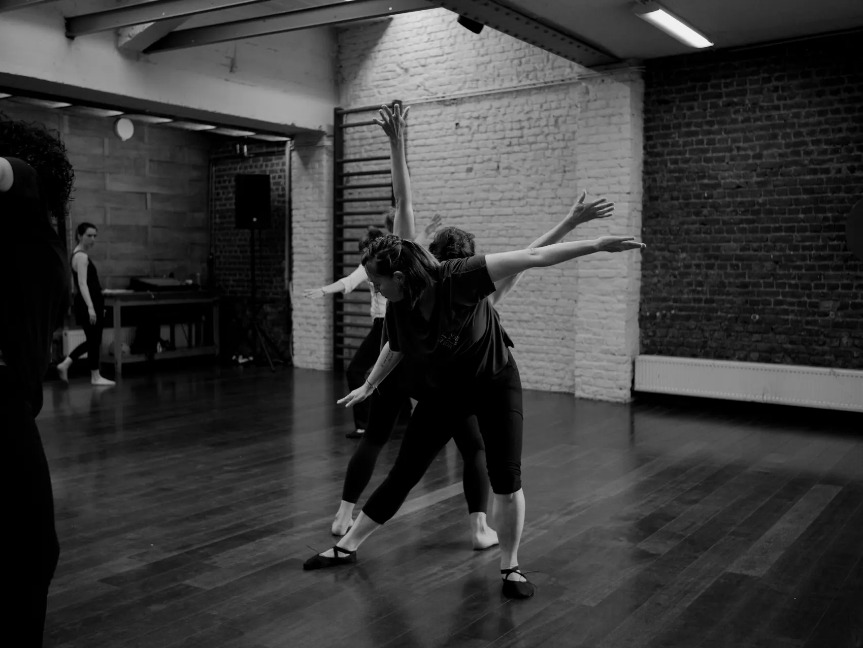 Twee danseressen met geopende armen in een studio met bakstenen muren