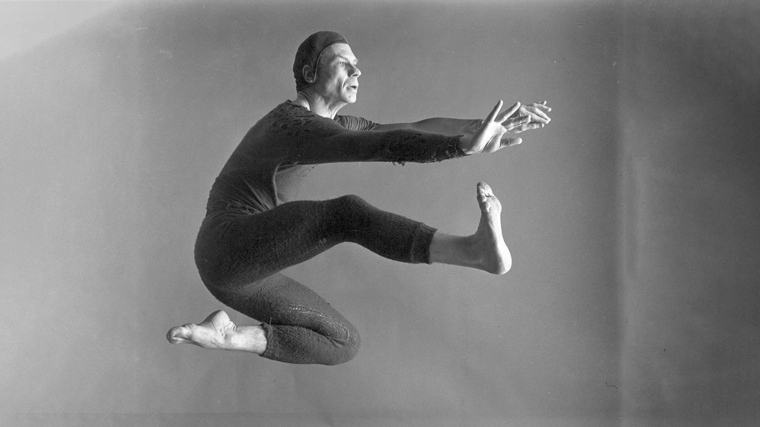 Merce Cunningham saute, les bras tendus devant lui, sur une photographie en noir et blanc